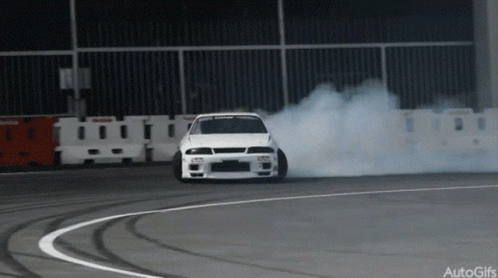 A White Car Is Drifting On A Track And Smoke Is Coming Out Of The Tire GIF