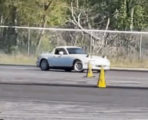 A White Car Is Drifting On A Track Next To Yellow Cones . GIF