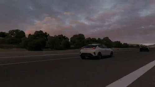 A White Car Is Driving Down A Highway With Trees In The Background GIF