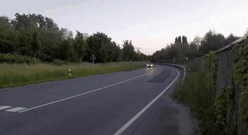 A White Car Is Driving Down A Road With A Fence In The Background GIF