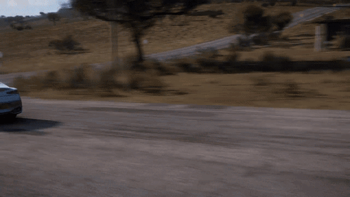 A White Car Is Driving Down A Road With A Grassy Hill In The Background GIF