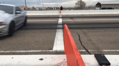 a white car is driving down a road with a red barrier in the foreground