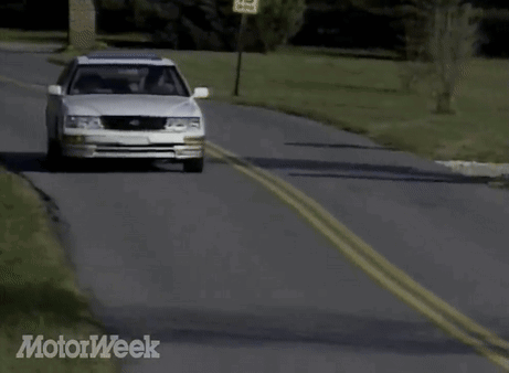 A White Car Is Driving Down A Road With Motorweek Written In The Corner GIF