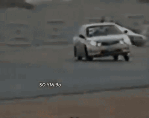 A White Car Is Driving Down A Road With The Words Sc Ym 90 On The Bottom Right Corner . GIF