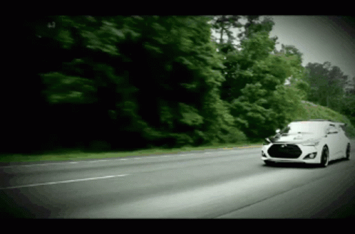 A White Car Is Driving Down A Road With Trees On The Side GIF