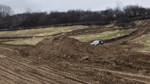 A White Car Is Driving Through A Dirt Field With A Fence In The Background GIF