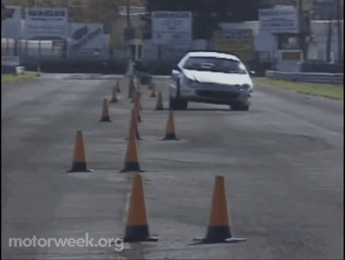 A White Car Is Driving Through A Row Of Orange Traffic Cones With Motorweek.org Written On The Bottom Right GIF