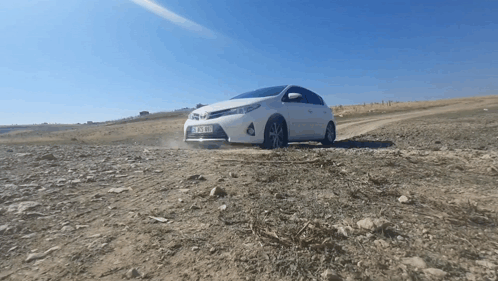 A White Car With A License Plate That Says ' Tk Xm ' On It Is Driving On A Dirt Road GIF