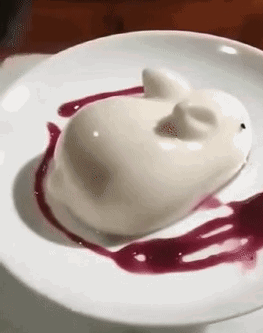 A White Dessert In The Shape Of A Cat On A White Plate With A Purple Sauce . GIF