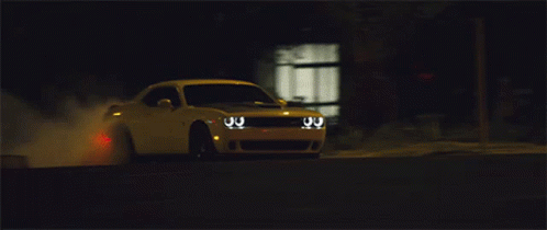 A White Dodge Challenger Driving Down A Street At Night GIF