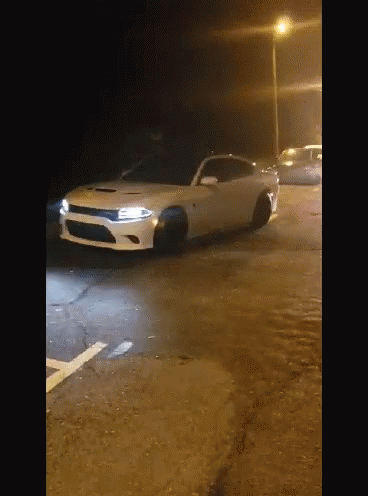 A White Dodge Charger Is Parked On The Side Of The Road At Night GIF