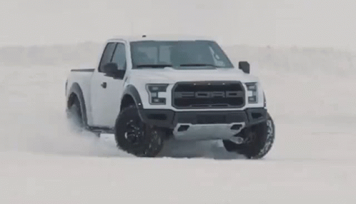 A White Ford Raptor Truck Is Driving In The Snow . GIF