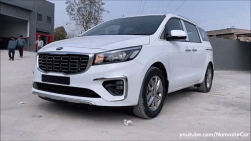 A White Kia Minivan Is Parked In A Parking Lot In Front Of A Building GIF