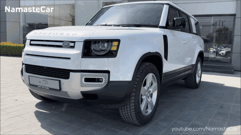 A White Land Rover Defender Is Parked In Front Of A Namaste Car Dealership GIF