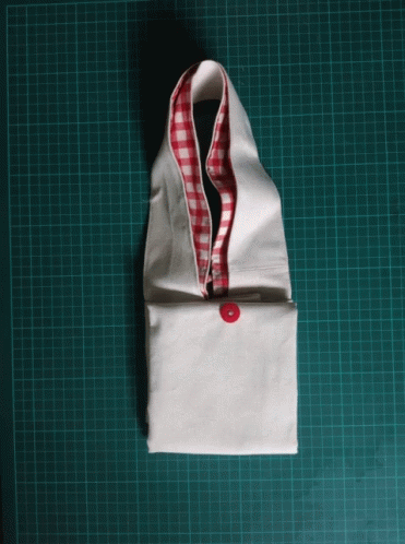 A White Piece Of Fabric With A Red And White Checkered Collar Is Sitting On A Green Cutting Board GIF