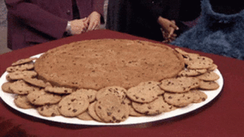 A White Plate Filled With Chocolate Chip Cookies And A Giant Cookie GIF