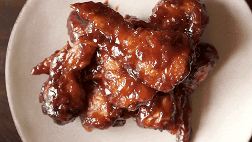 A White Plate Topped With Chicken Wings Covered In A Brown Sauce GIF