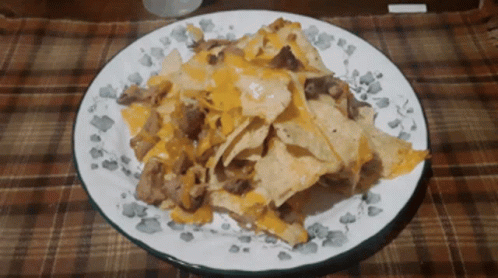 A White Plate Topped With Nachos And Cheese GIF