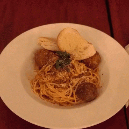 A White Plate Topped With Spaghetti Meatballs And Bread GIF