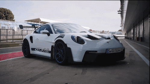 A White Porsche Gt3rs Is Parked On A Race Track GIF