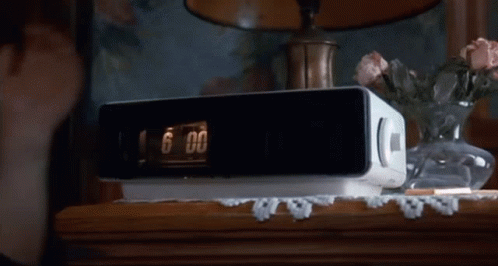 A White Radio Is Sitting On A Wooden Table Next To A Vase Of Flowers GIF