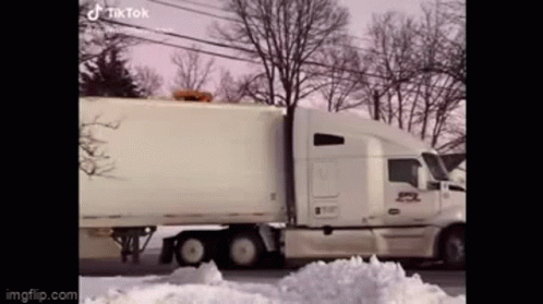 A White Semi Truck Is Driving Down A Snowy Street . GIF