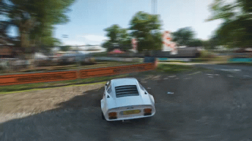 A White Sports Car Is Driving Down A Dirt Road With A Fence Behind It GIF