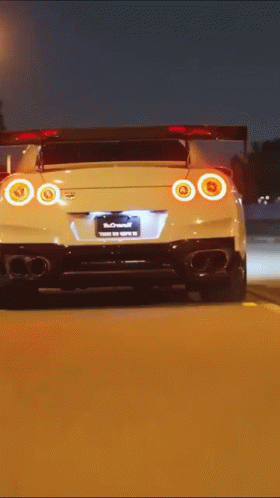 A White Sports Car Is Driving Down A Road At Night GIF