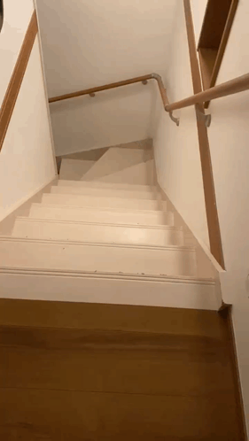 A White Staircase With A Wooden Railing And A Wooden Floor GIF