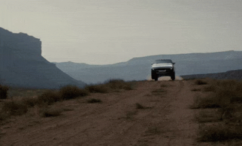 A White Truck Is Driving Down A Dirt Road GIF