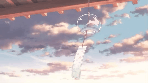 A Wind Chime With A Rabbit On It Is Hanging From A Roof With A Cloudy Sky In The Background . GIF
