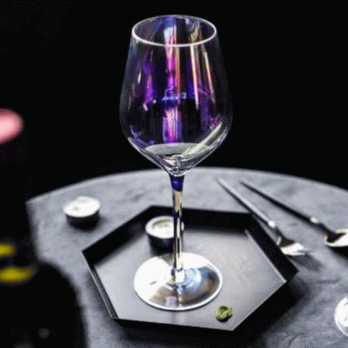 A Wine Glass With A Purple Stem Is Sitting On A Black Plate On A Table . GIF