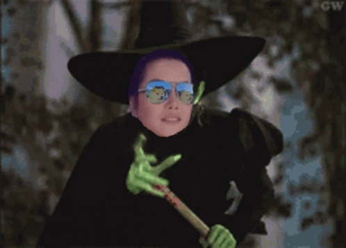 A Witch Wearing Sunglasses And A Purple Hat Is Holding A Green Wand GIF