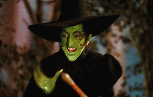 A Witch With Green Face Paint And A Black Hat Holds A Broom GIF