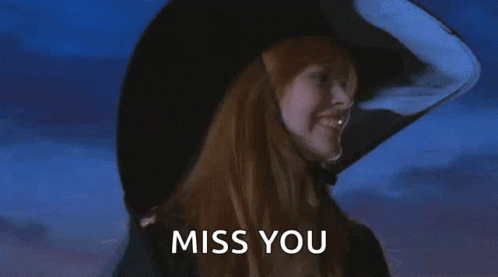 a witch with red hair is wearing a large black hat and says miss you .