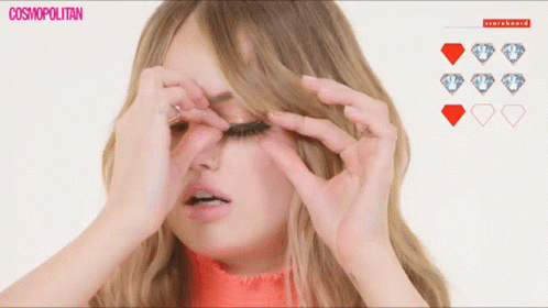 A Woman Adjusts Her Eyelashes In Front Of A Scoreboard With Diamonds GIF