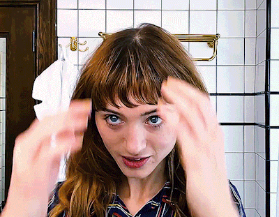 A Woman Adjusts Her Hair In A Bathroom With A Towel Hanging On The Wall GIF
