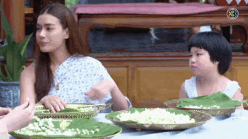 A Woman And A Child Are Sitting At A Table With Plates Of Food . GIF
