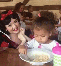 A Woman And A Little Girl Are Sitting At A Table With A Bowl Of Food In Front Of Them GIF
