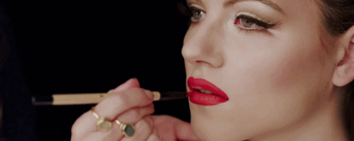 A Woman Applies Red Lipstick To Her Lips With A Brush GIF