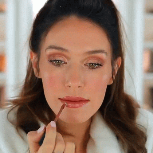 A Woman Applying Lip Gloss To Her Lips With A Brush GIF