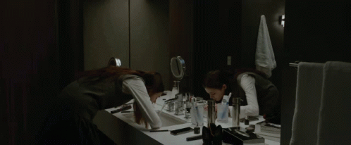 A Woman Applying Makeup In Front Of A Mirror In A Bathroom GIF