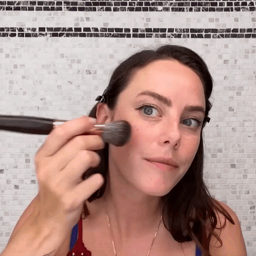 A Woman Applying Makeup With A Brush On Her Face GIF