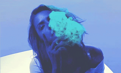 A Woman Blowing Blue Smoke From Her Mouth While Giving The Middle Finger GIF