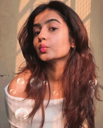 A Woman Blowing Bubbles In Front Of Her Face GIF