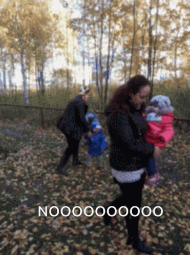 A Woman Carrying A Baby In A Park With The Word Nooo On The Bottom Left GIF