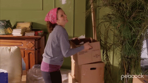 A Woman Carrying A Box With The Word Peacock On The Bottom Right GIF