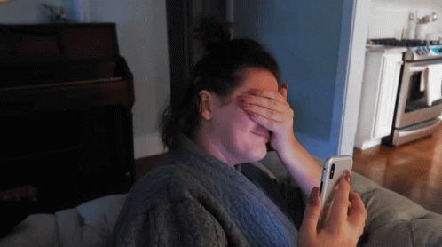 a woman covering her eyes with her hand while looking at her cell phone
