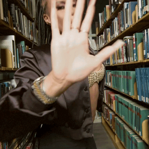 A Woman Covering Her Face In A Library With A Book Called Angels GIF