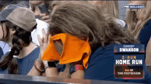 A Woman Covering Her Face With An Orange Towel While Watching A Baseball Game GIF